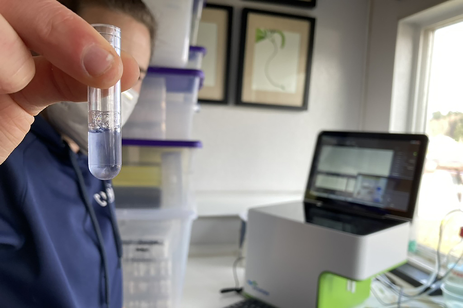 A person holds a test tube in front of a laptop computer