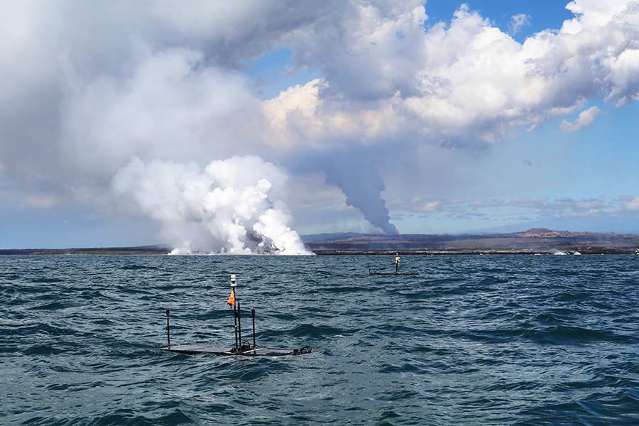 A device floats on the water with plumes of smoke and clouds in the distance