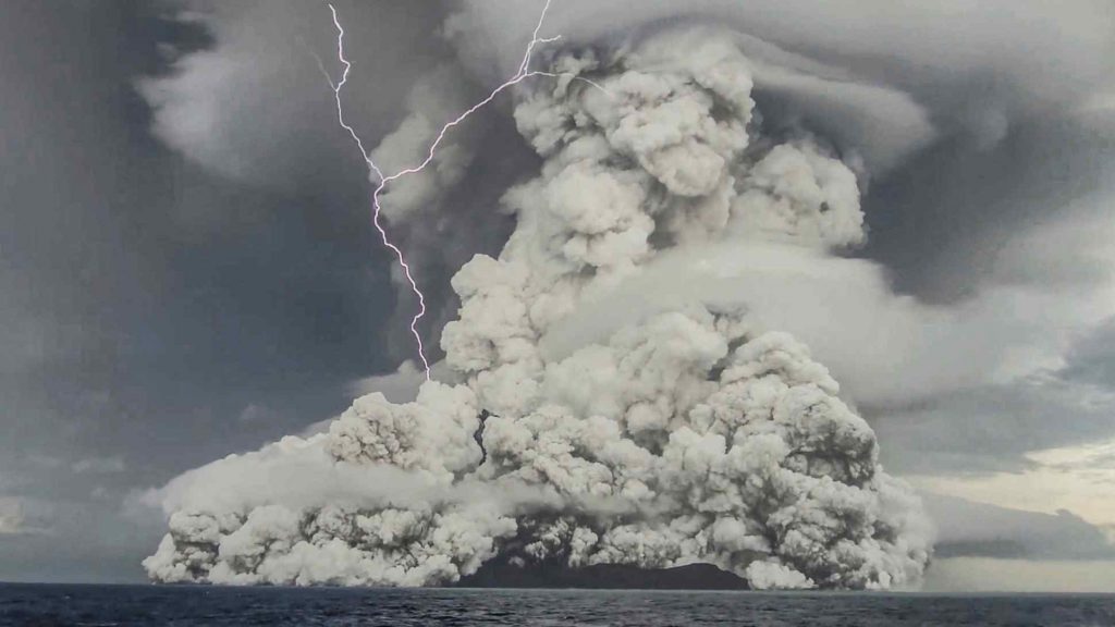 dark grey smoke plume stemming from volcano in ocean