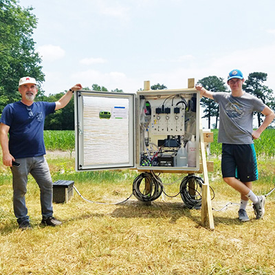 Photo of two engineers standing next to water monitoring equipment in field