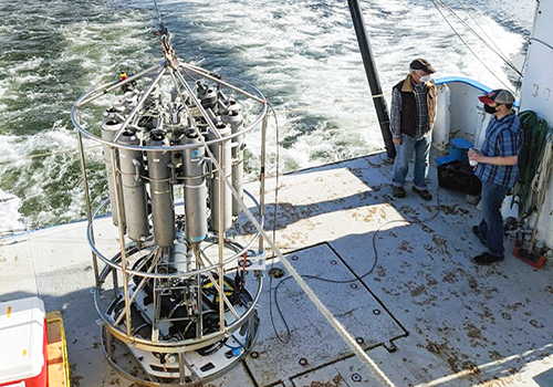 Photo of two men working with an ocean monitoring device on a ship deck