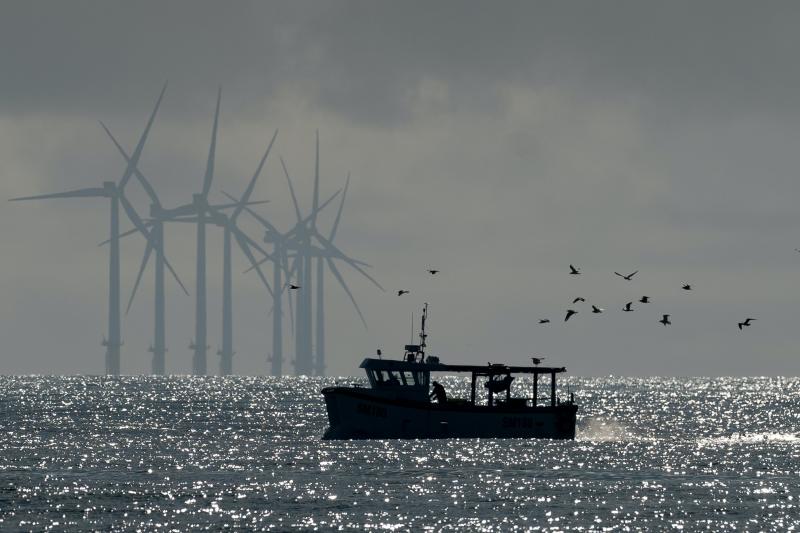 A fishing vessel on the ocean with windmills and sea gulls in the background