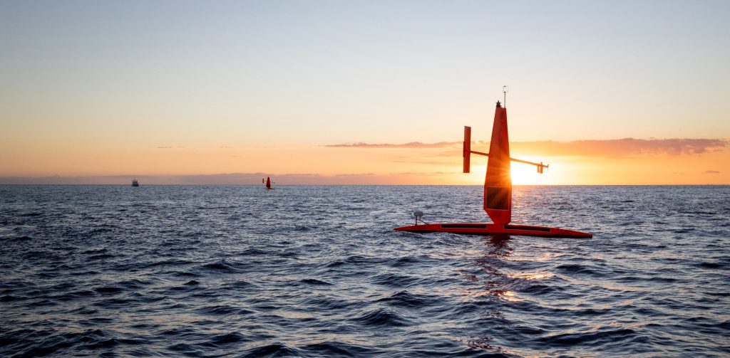 Two saildrones upon the ocean with a sunset