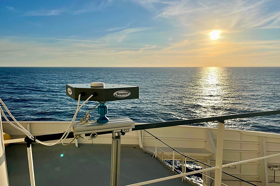 An instrument mounted on the top of an ocean vessel with ocean and sunset in the distance