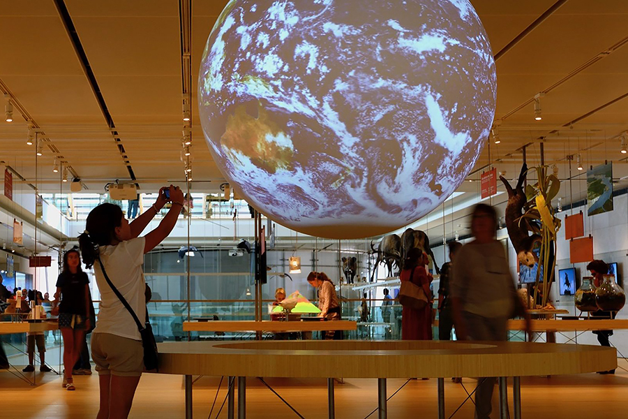 A person stands near a spherical digital projection of Earth