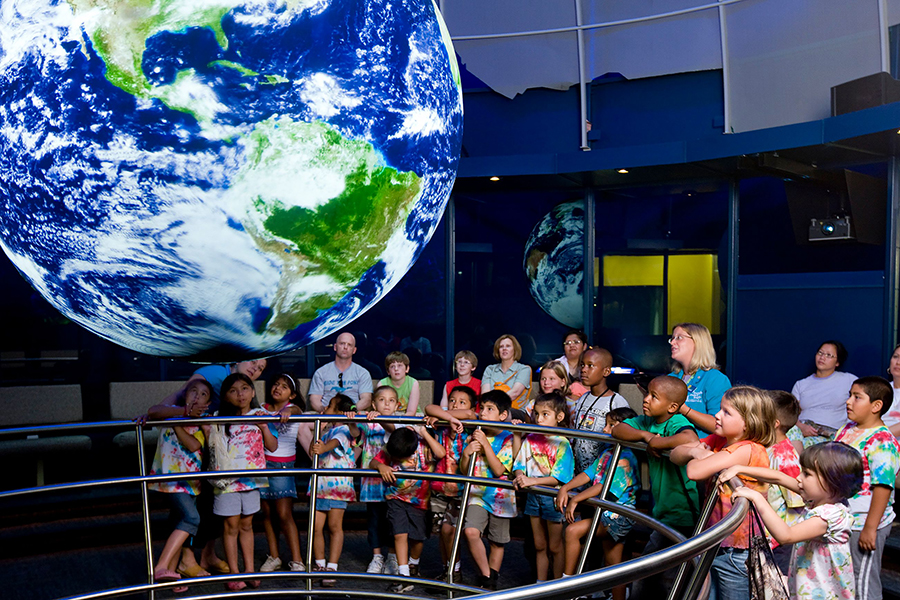 A group of children look up at a digital globe projection