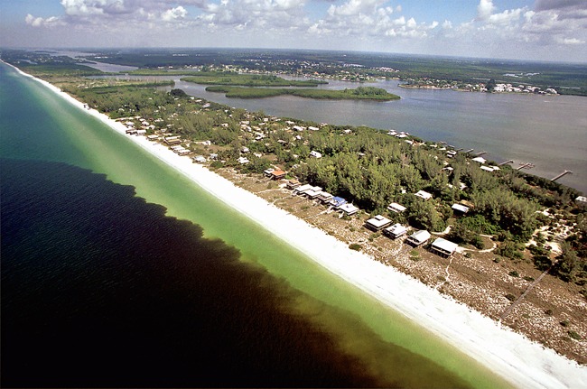 An aerial shot of a beachfront community with a dark red wave in the ocean